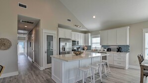 A modern kitchen with white cabinetry, a large island with bar stools, and a breakfast bar. - < 1 Mi to Sea Isle Beach: Home w/ Pool Access (Galveston)