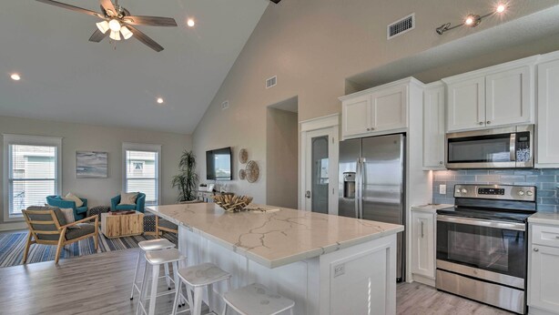 A spacious kitchen with white cabinets, a large island with stools, stainless steel appliances, and a ceiling fan. - < 1 Mi to Sea Isle Beach: Home w/ Pool Access (Galveston)