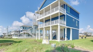 A two-story beach house with a balcony, a covered porch, and a staircase leading to the upper level.