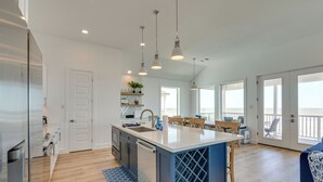 A modern kitchen with a central island, pendant lighting, and a view to a balcony.
