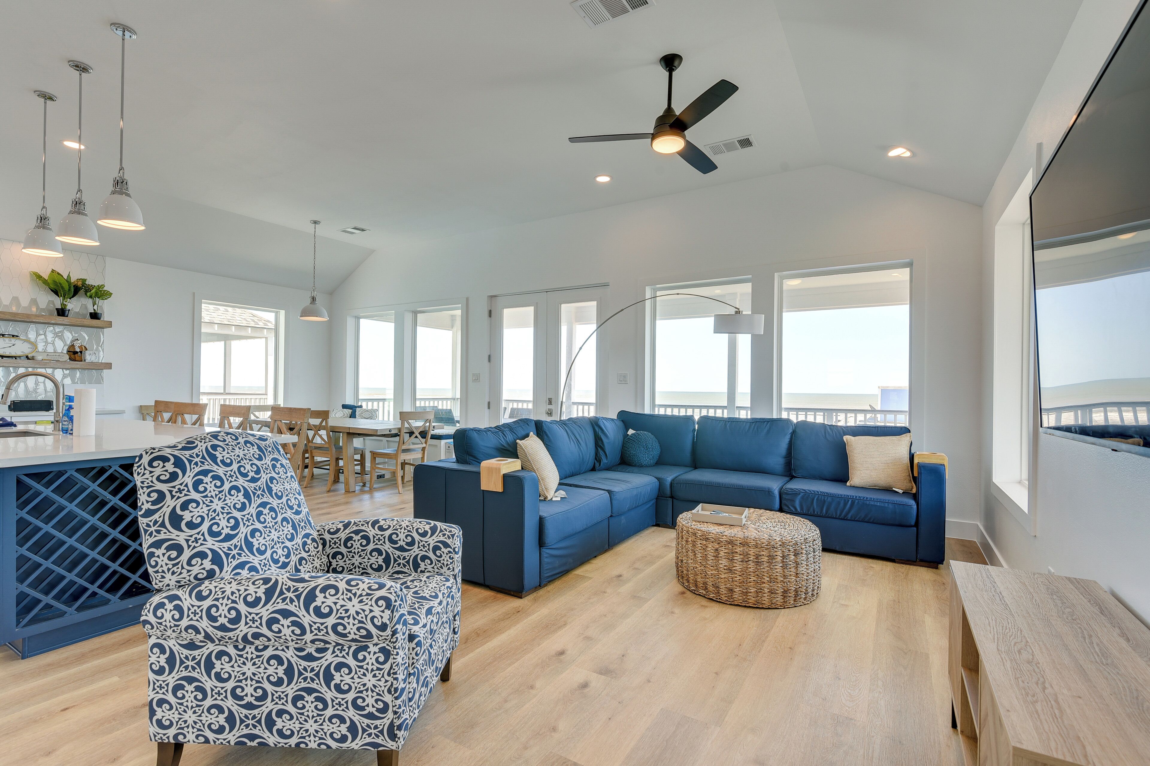 A spacious living area with a blue sectional sofa, a patterned armchair, a wooden coffee table, and a ceiling fan.