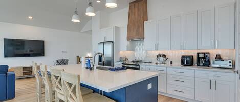 A modern kitchen with a central island, white cabinetry, and a large flat-screen TV mounted on the wall.