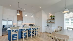 A modern kitchen with a central island, wooden chairs, and pendant lighting.