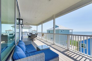 A balcony with blue cushions, wicker furniture, and a view of the ocean and beach houses. - Ocean Views, Steps to Sand! Coastal Galveston Gem (Galveston)