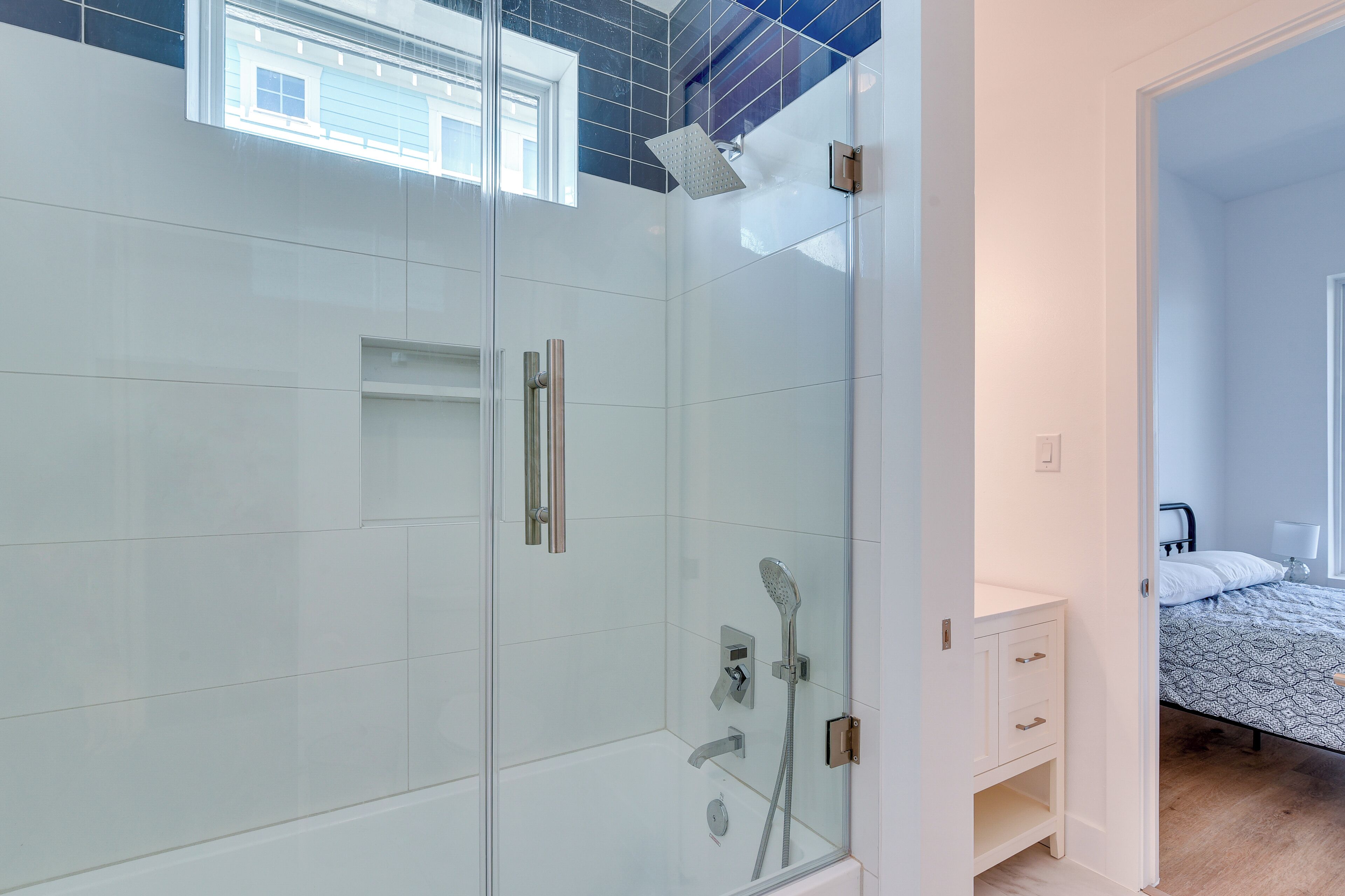 A modern bathroom with a glass shower enclosure, a white vanity, and a bed with patterned bedding.