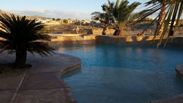 En swimmingpool med buet kant, palmer og et fjerntliggende udsyn til huse.