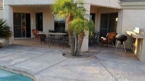 Un'area patio esterna con piscina, tavolo e sedie, barbecue e una palma.