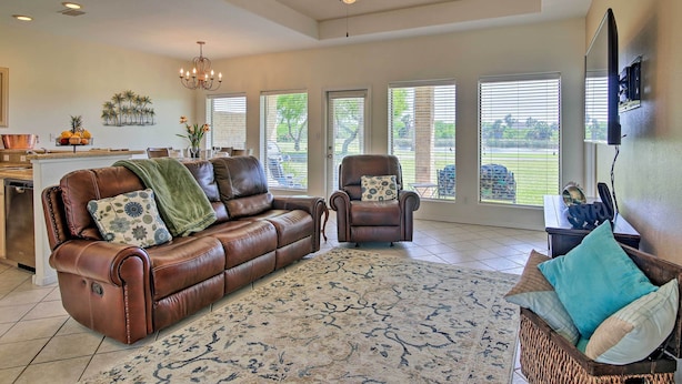 A spacious living room with a brown leather sofa, a patterned rug, and a large window with blinds.