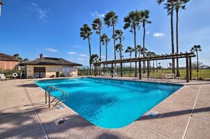 A swimming pool with a pergola, palm trees, and a building in the background.