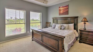 A bedroom with a large bed, a ceiling fan, a nightstand, a lamp, and two windows with blinds.