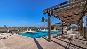 A pool area with a wooden pergola, lounge chairs, and a table.