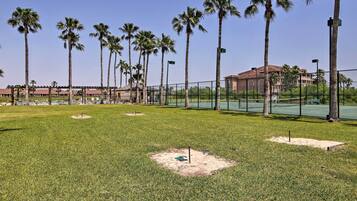 A grassy area with palm trees and a fenced tennis court.