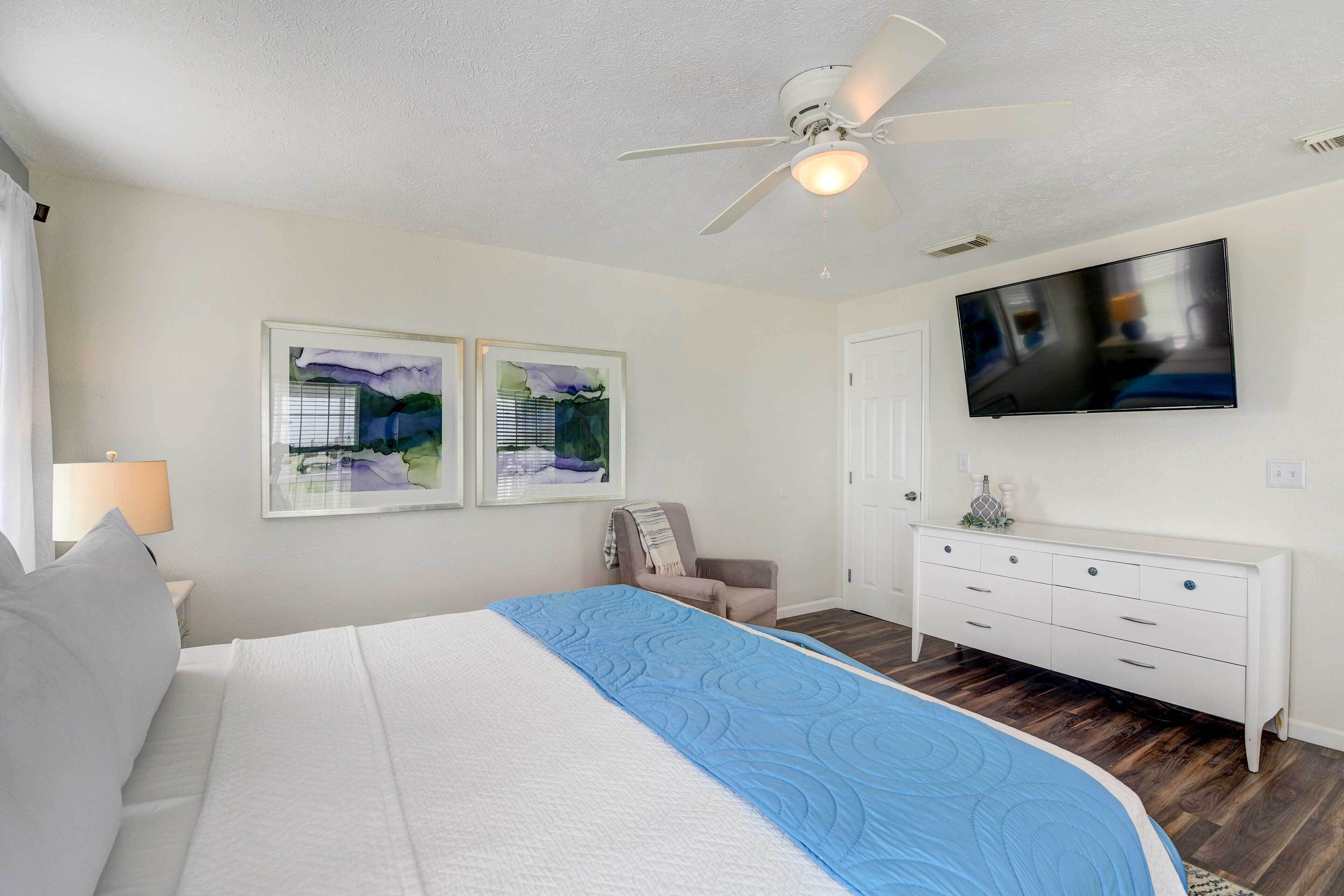 A bedroom with a bed, a ceiling fan, a TV, a dresser, and two framed pictures on the wall.