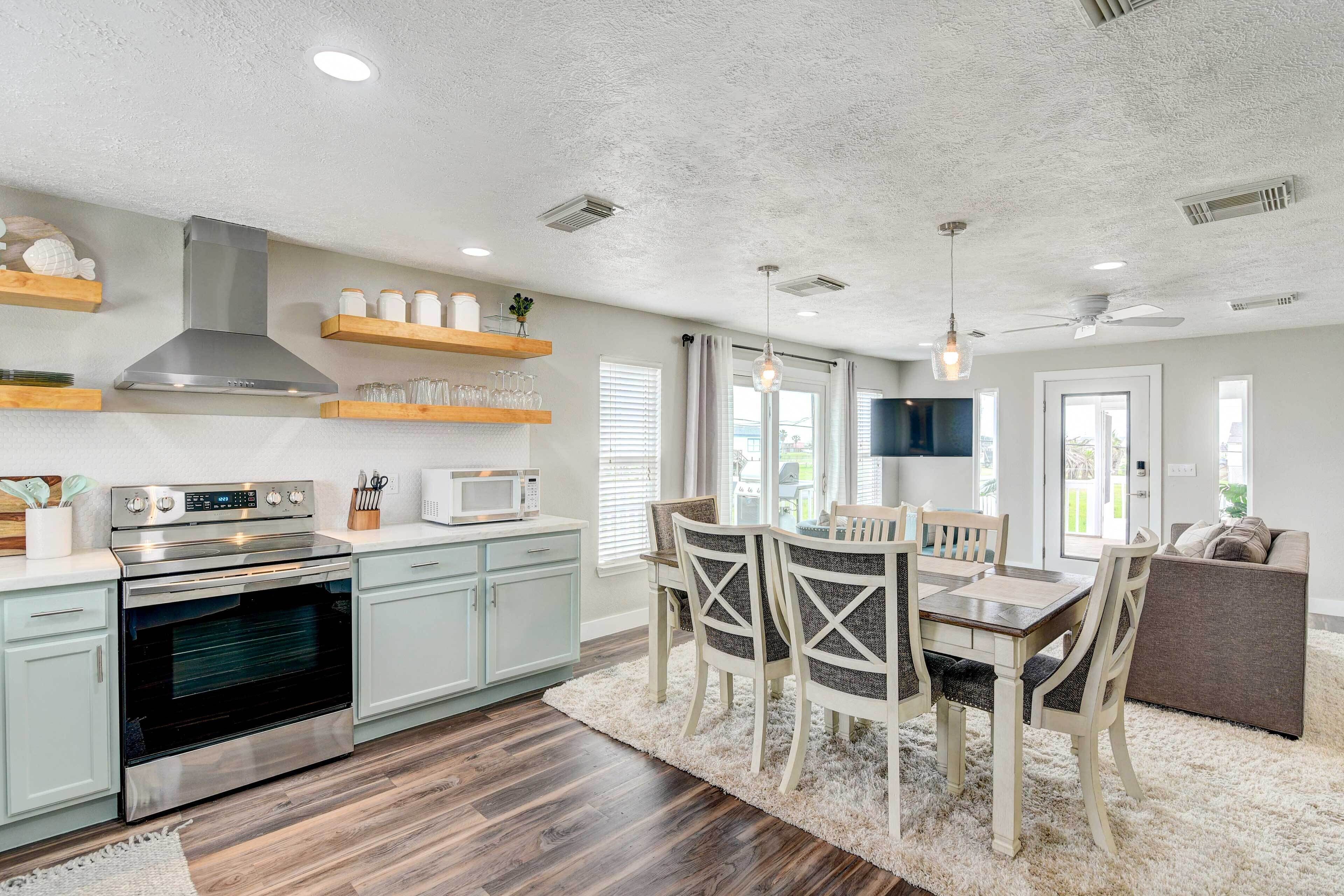 A modern kitchen with a stainless steel range, microwave, and oven. There is a dining area with a table and chairs, and a large window providing natural light.