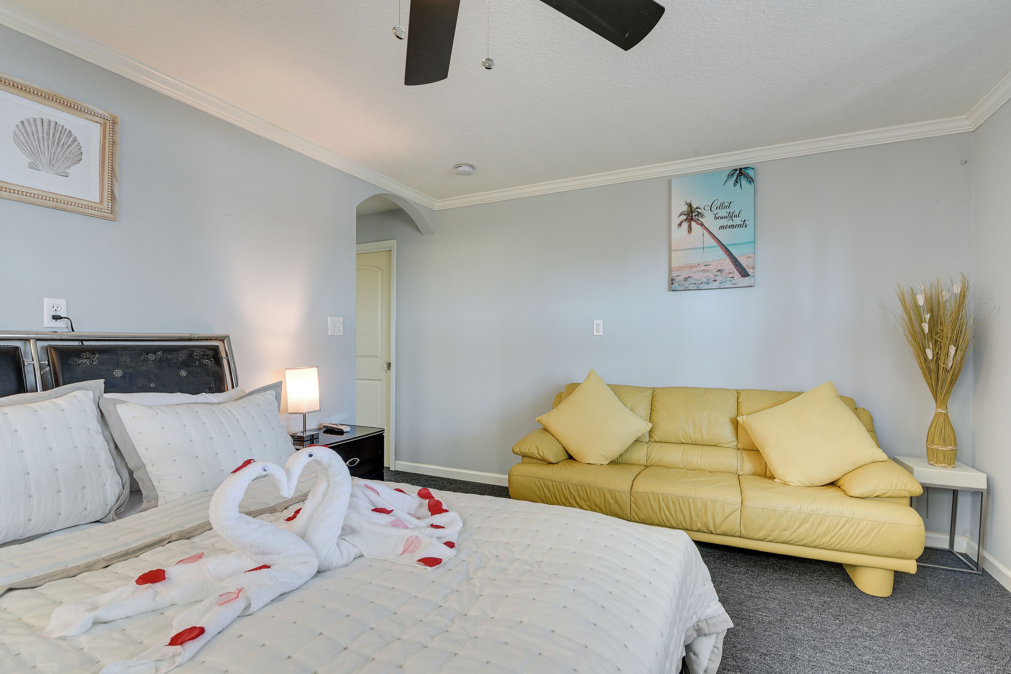 Une chambre d’hôtel avec un lit, un canapé jaune, un tableau encadré au mur et un vase contenant des plantes séchées.