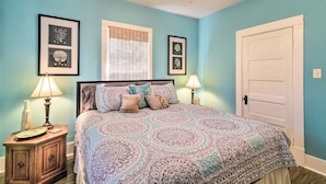 A bedroom with a bed, bedside lamps, a nightstand, a window with blinds, and framed artwork on the walls. - 2 Mi to Beach & Seawall! Coastal Winter Escape (Galveston)