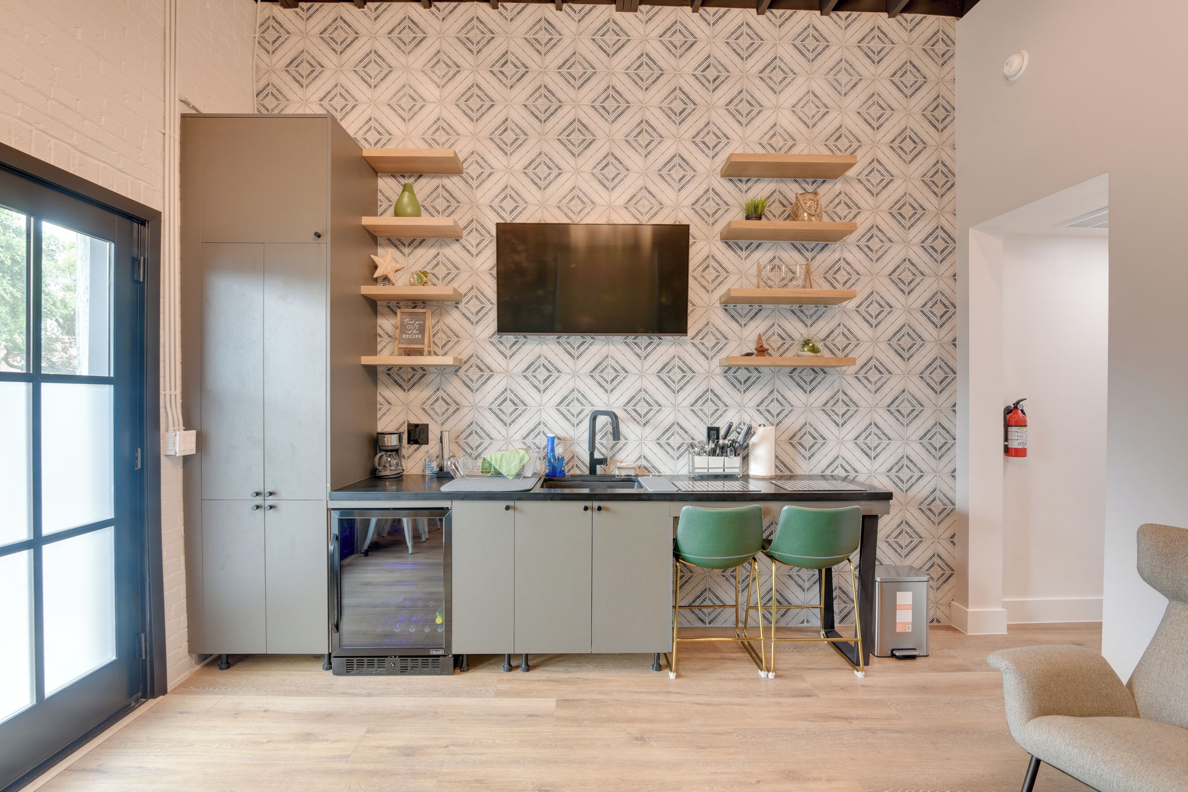 A modern kitchen with a built-in dishwasher, a large flat-screen TV, and a dining area with two green chairs.