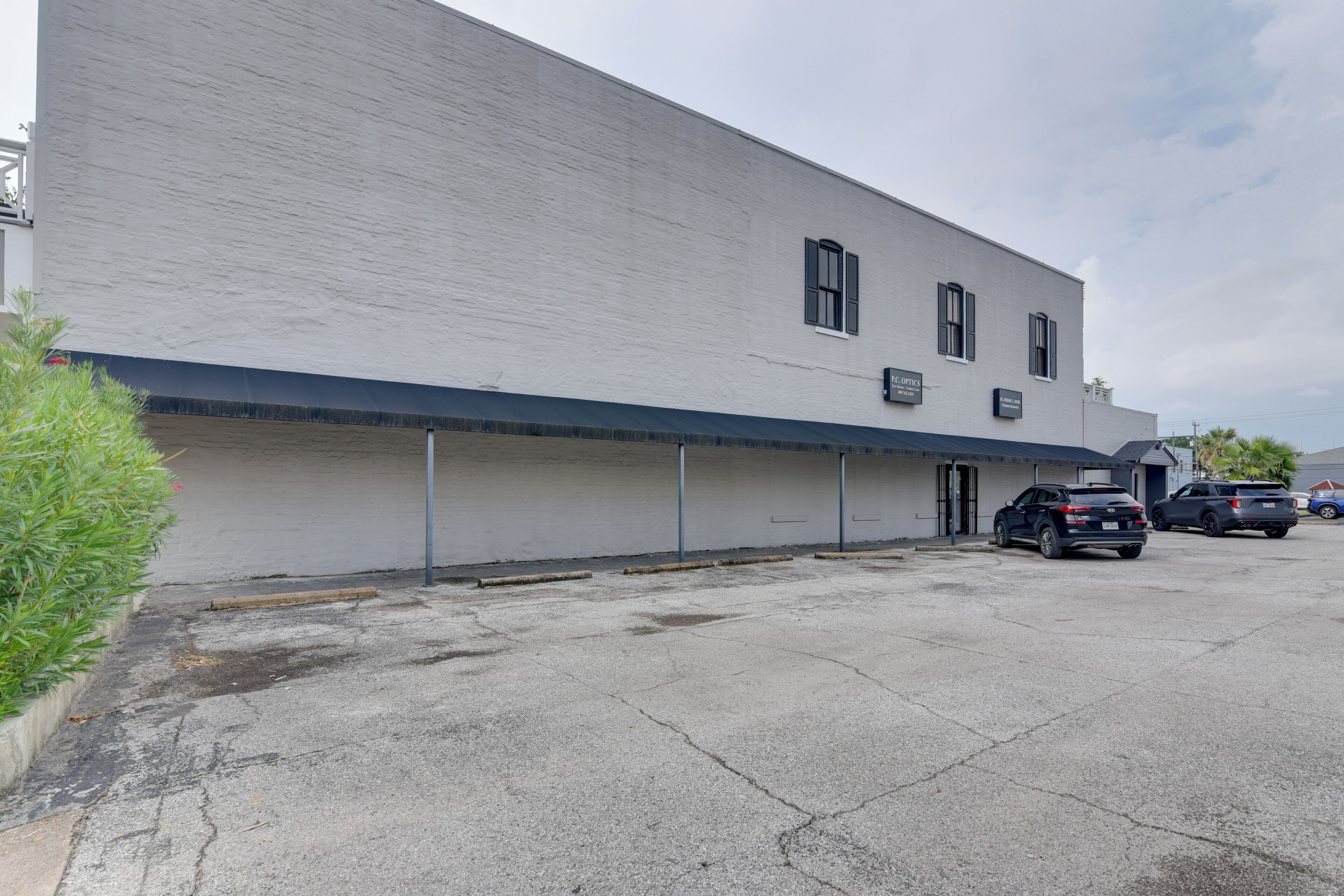 A two-story building with a flat facade, a covered entrance, and a parking lot with several cars.