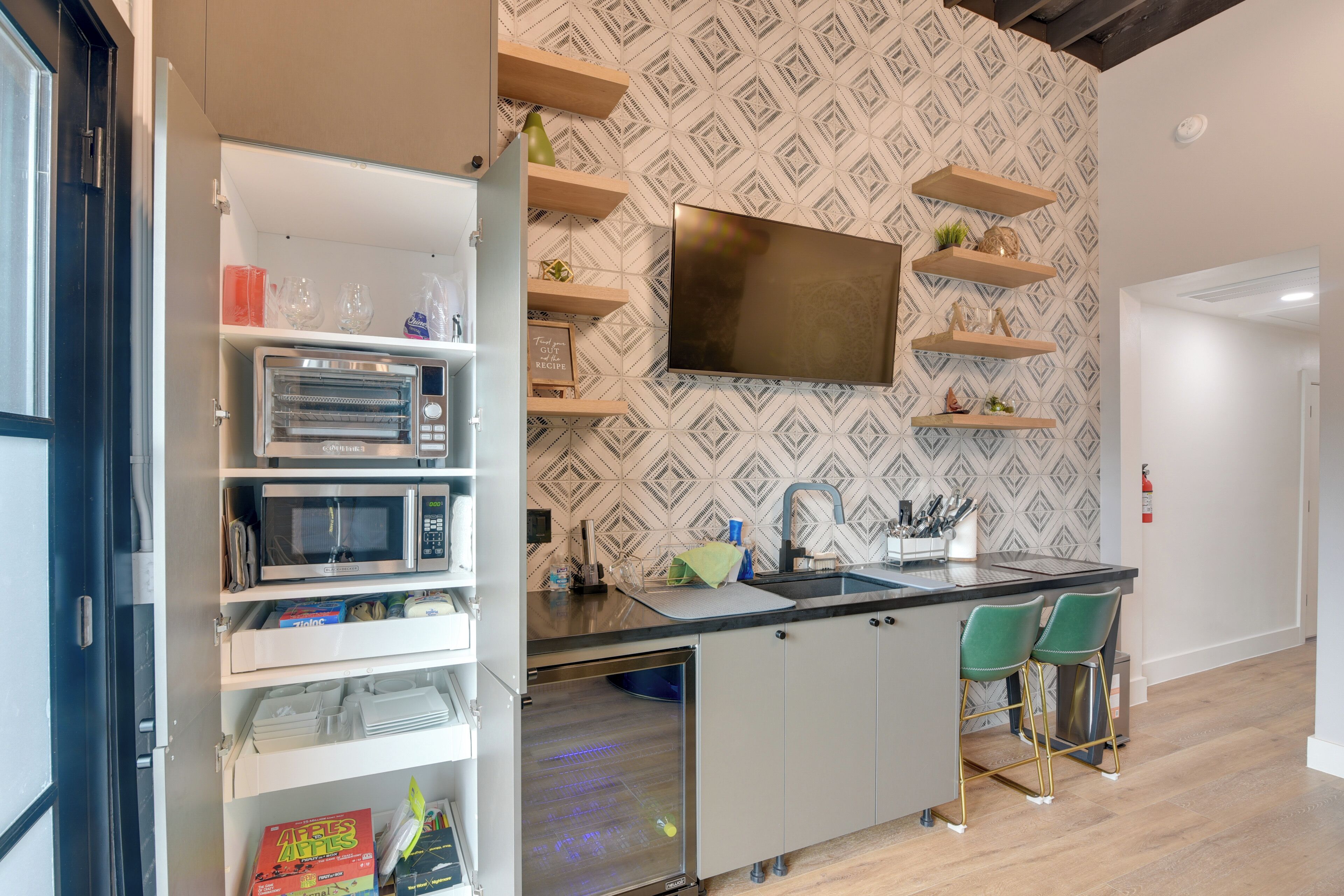 Cozinha moderna com eletrodomésticos embutidos, TV de tela plana e área de bar com banquetas.