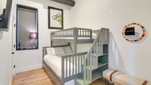 Une chambre avec un lit superposé, une fenêtre, un tableau encadré, un miroir et un banc.