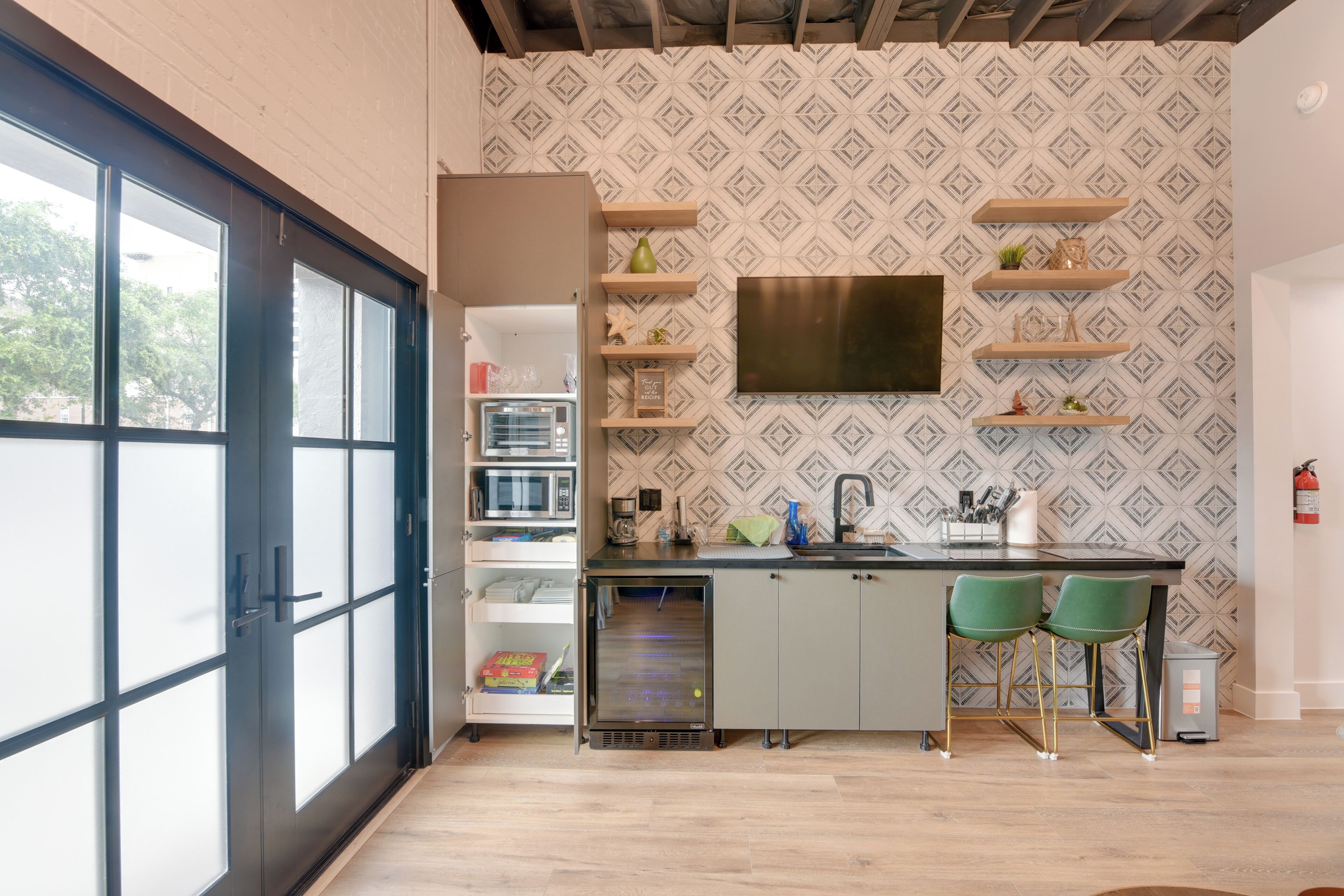 Una cocina moderna con refrigerador empotrado, microondas y pileta. Hay dos taburetes verdes y un ventanal que proporciona luz natural.