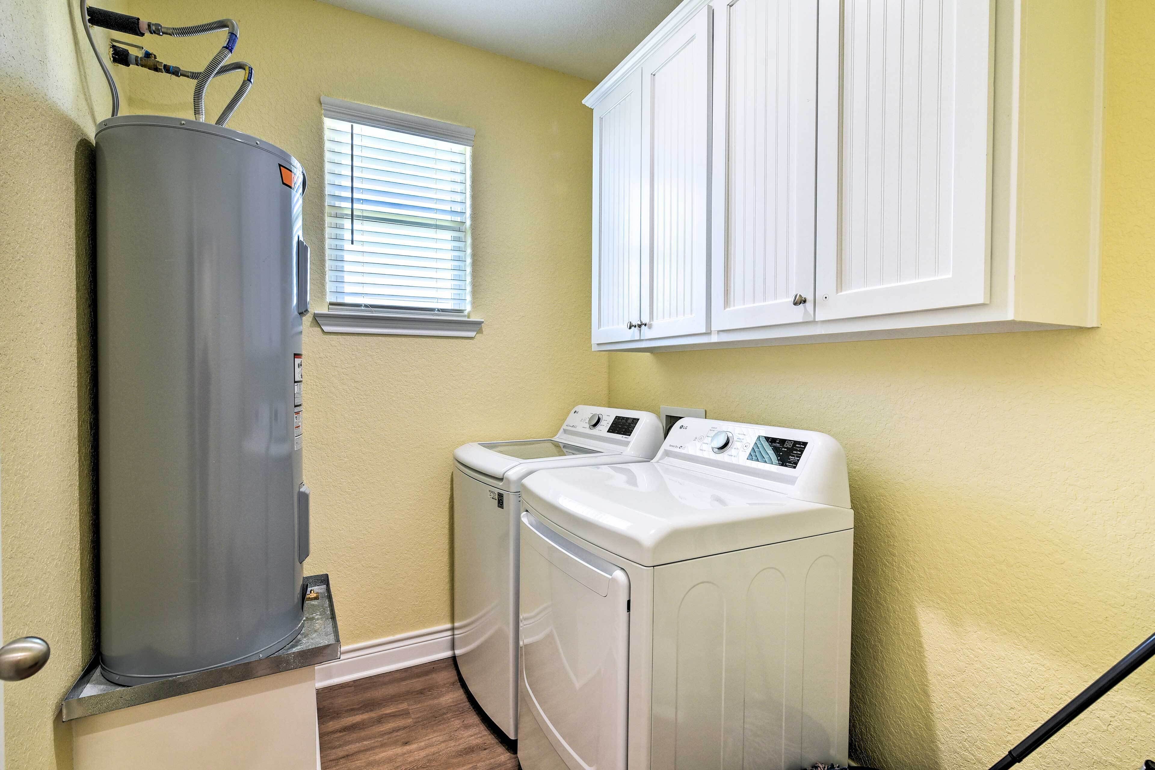 A laundry room with a gray water heater, two white front-loading washers, and a white cabinet above.