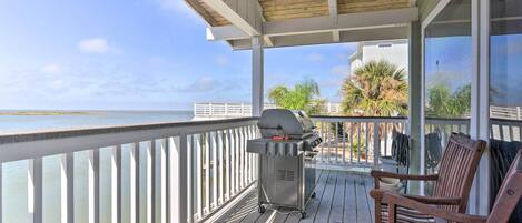Une terrasse couverte avec un barbecue, des chaises en bois et une vue sur l’océan.