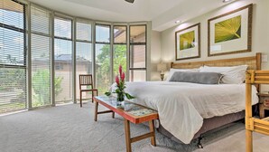 A bedroom with a bed, a wooden bench, a vase with flowers, and large windows with blinds. - Bright & Airy Lahaina Condo - Walk to Beach! (Kapalua)
