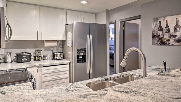 A modern kitchen with white cabinets, a stainless steel refrigerator, a built-in oven, and a granite countertop. - Brian Head Ski-in/ski-out Condo w/ Resort Perks! (Brian Head)