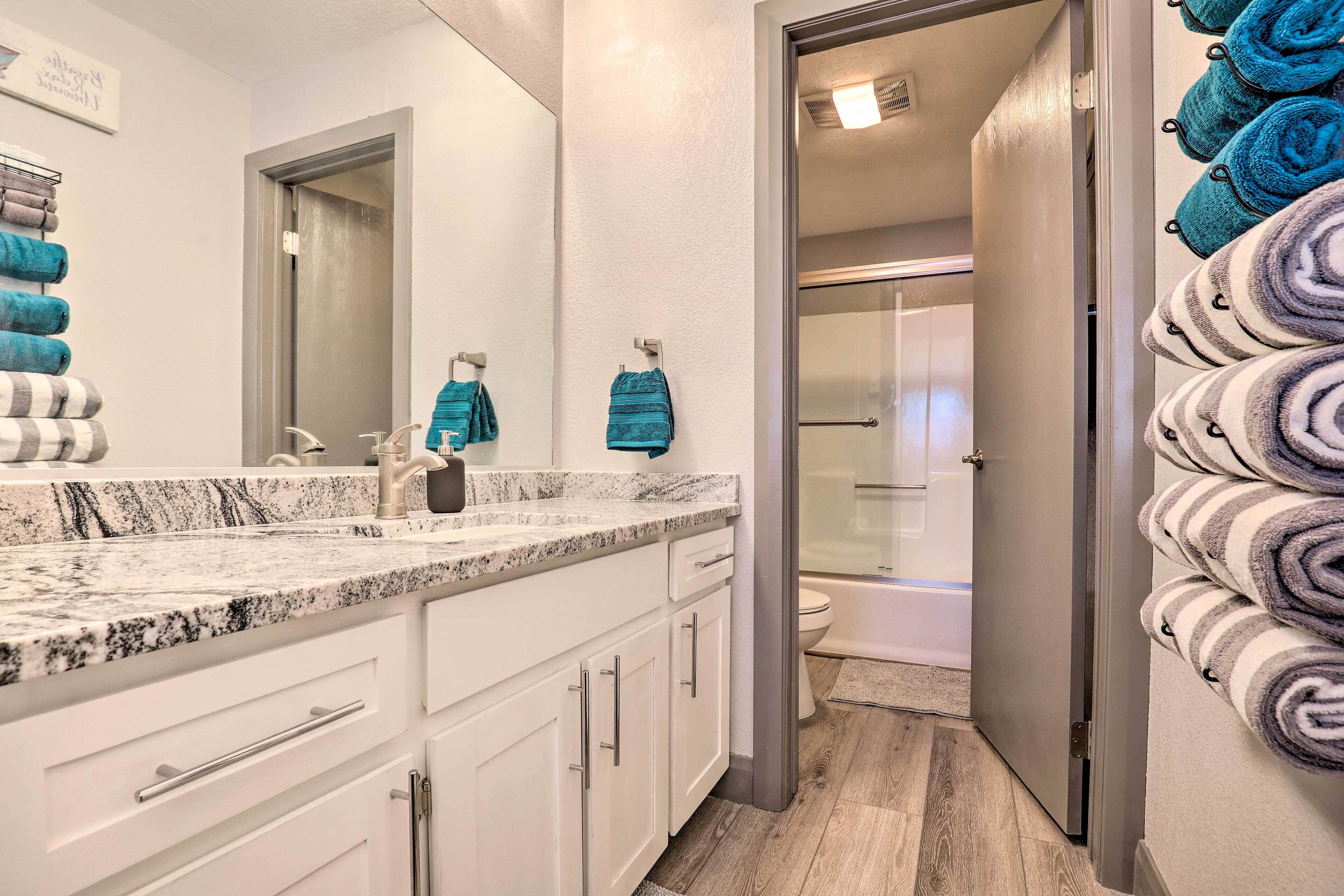 A bathroom with a marble countertop, white cabinets, a sink, and a glass shower enclosure.