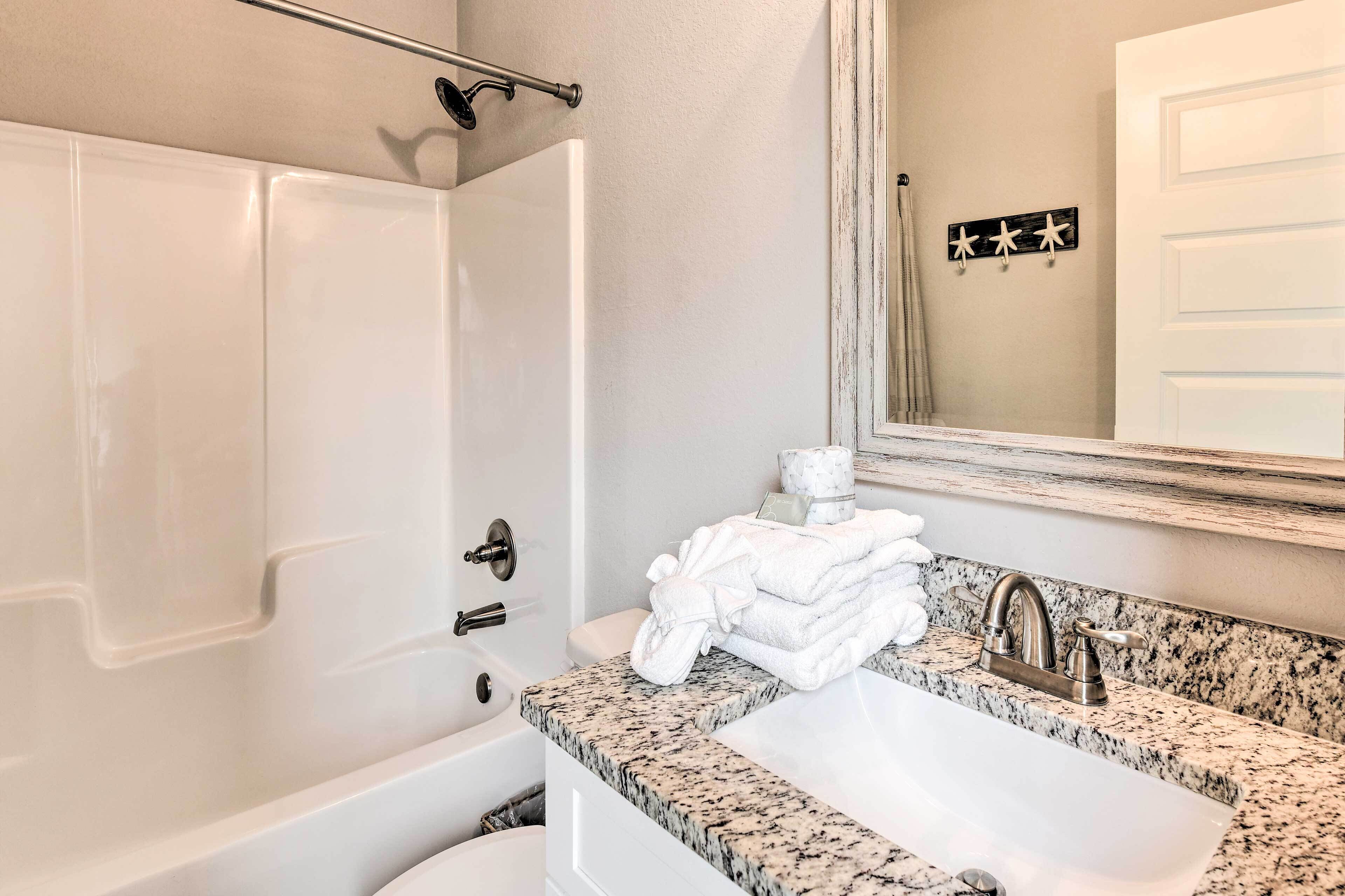 A bathroom with a bathtub, a sink with a granite countertop, and a mirror above the sink.