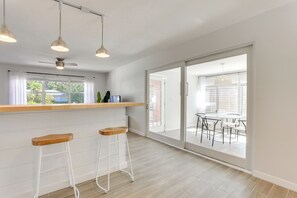 Een moderne keuken met een houten aanrecht, twee barkrukken, hanglampen en een glazen schuifdeur naar een terras.