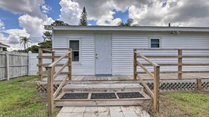 A white single-story house with a front door, a small window, and a wooden deck with a metal grate entrance. - Central Sarasota Home: 8 Mi to Siesta Key! (Sarasota)