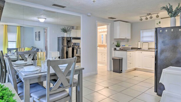 A modern kitchen with white cabinets, a stainless steel refrigerator, and a dining area with a table set for four. - Central Sarasota Home: 8 Mi to Siesta Key! (Sarasota)