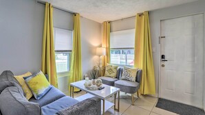 A living room with a sofa, armchair, and coffee table, yellow curtains, and a door. - Central Sarasota Home: 8 Mi to Siesta Key! (Sarasota)