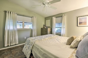 A bedroom with a bed, a ceiling fan, a dresser, and a window with curtains.