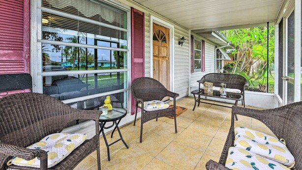 A covered porch with wicker furniture, a wooden door, and large windows. - North Port Escape w/ Pool ~ 12 Mi to Beach! (North Port)