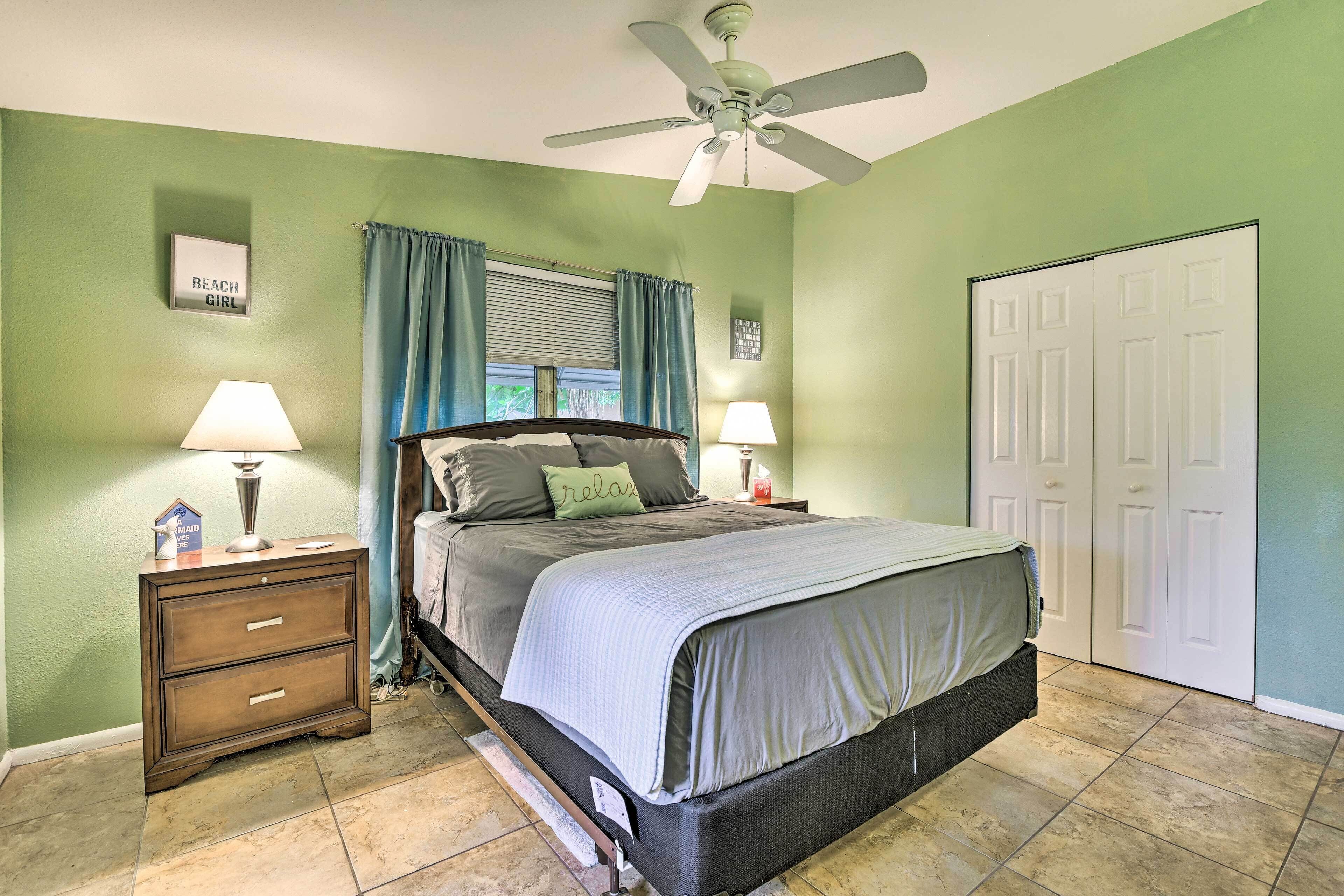 A bedroom with a bed, two bedside tables with lamps, a ceiling fan, a window with curtains, and a door.