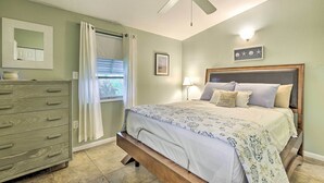 A bedroom with a bed, a dresser, a ceiling fan, a window with curtains, and a wall-mounted light fixture. - North Port Escape w/ Pool ~ 12 Mi to Beach! (North Port)