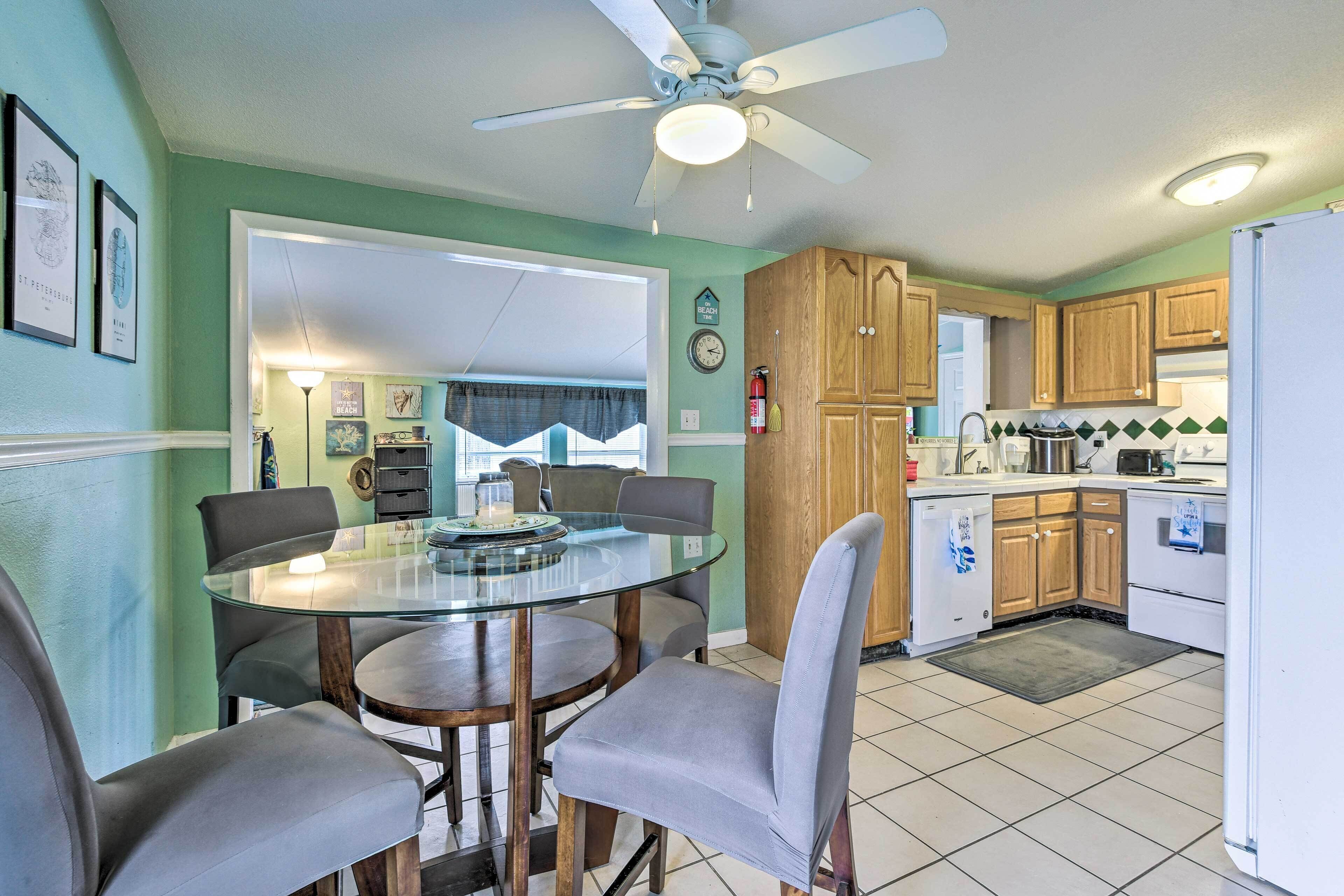 A compact kitchen with wooden cabinets, a glass dining table, and a ceiling fan.
