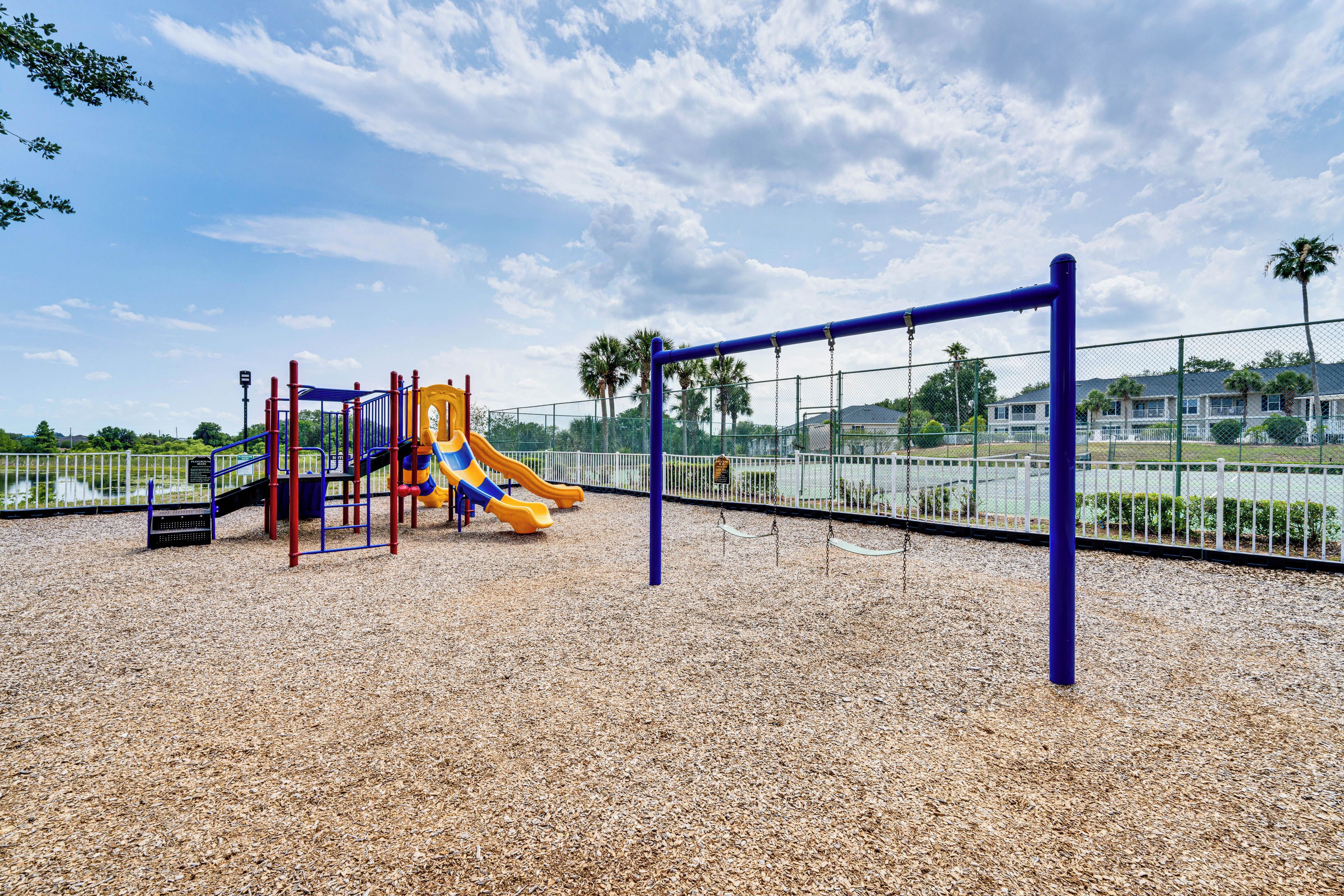 Un parque infantil con un tobogán y estructuras para escalar, rodeado por una valla y palmeras.