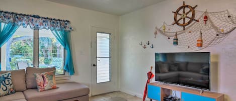 A living room with a sofa, coffee table, TV, and a wall decoration of a ship's wheel and net.