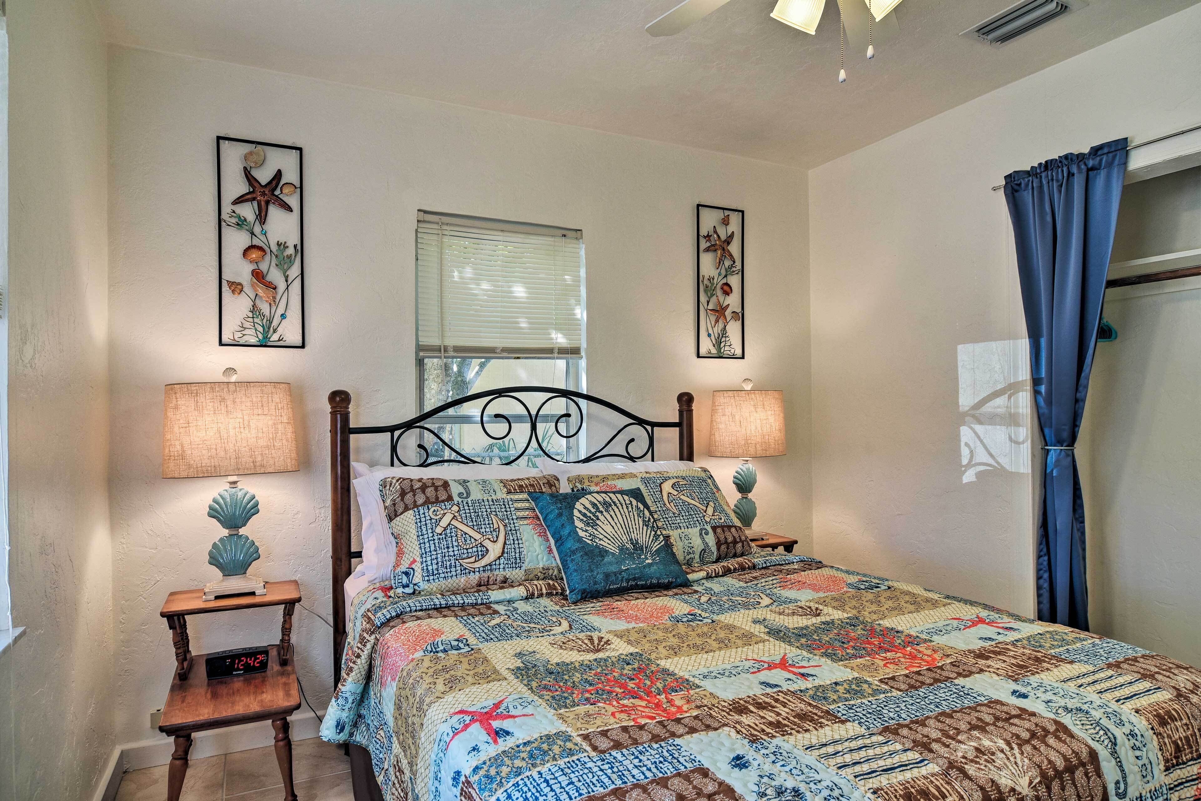 A bedroom with a bed, two bedside tables, a nightstand, a wall clock, and a window with curtains.
