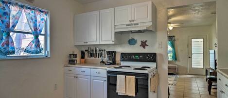 A kitchen with white cabinets, a stove, and a window with decorative curtains.