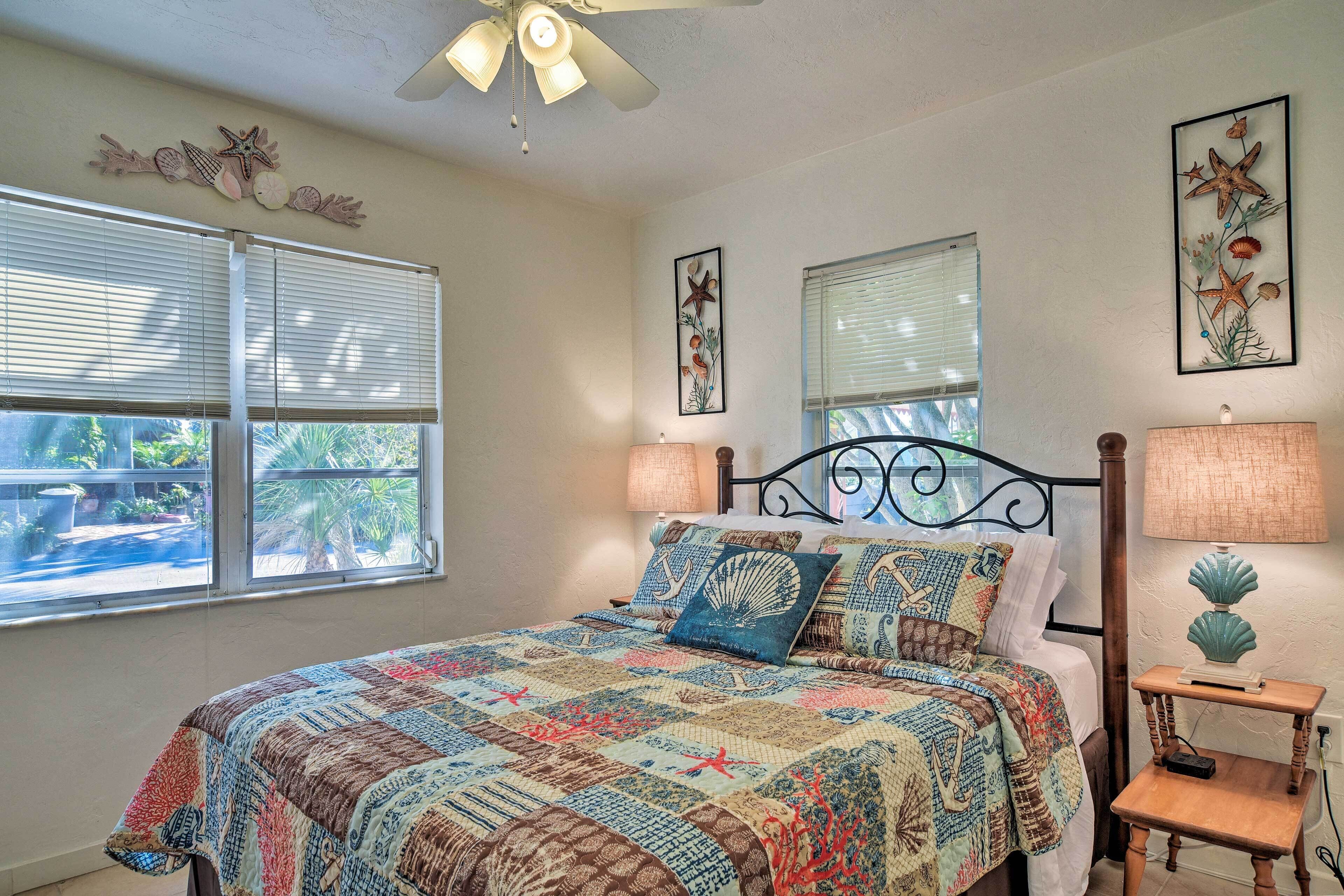 A bedroom with a bed, two windows, a ceiling fan, and wall art.