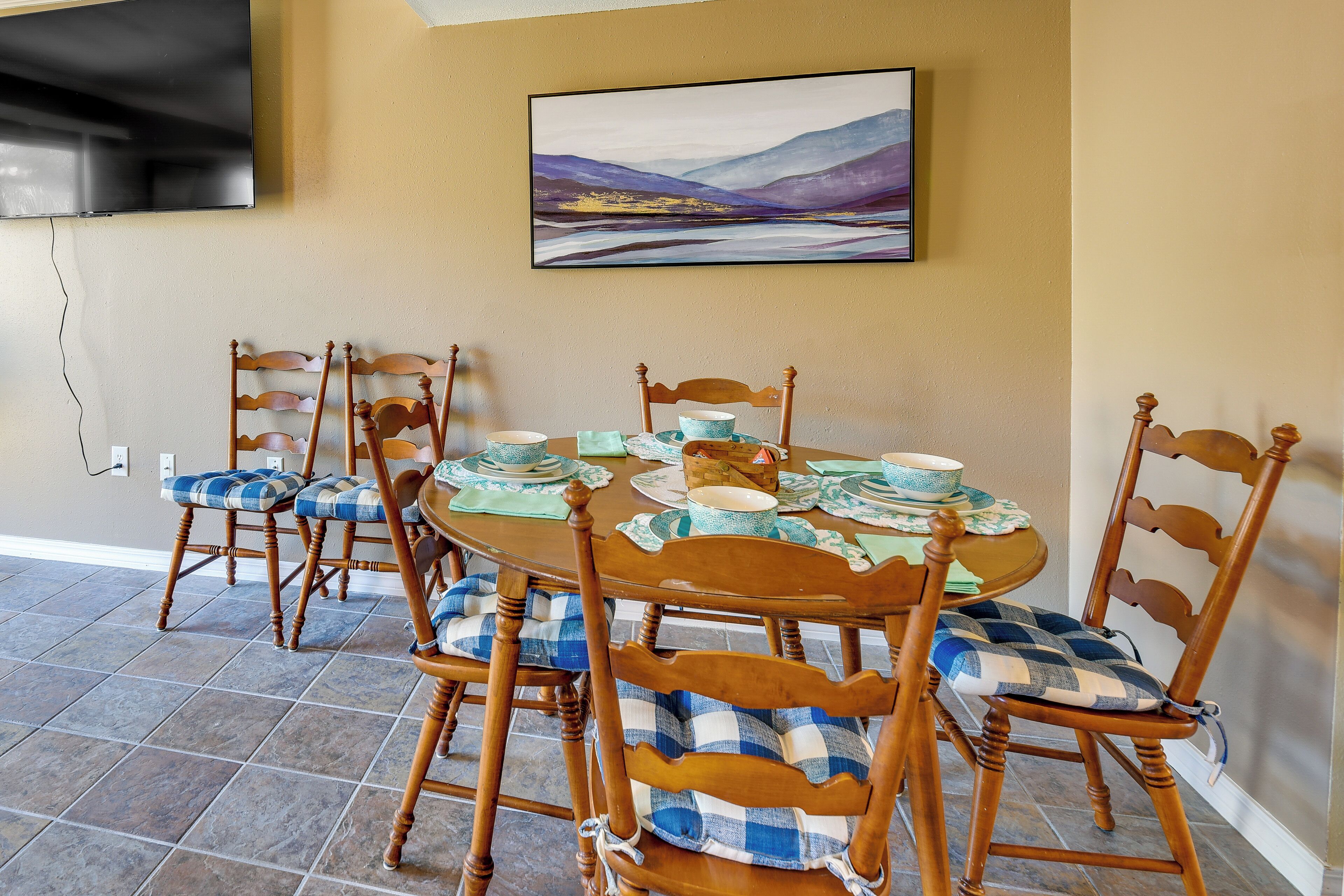 A dining area with a round table set for six, surrounded by wooden chairs with checkered cushions.