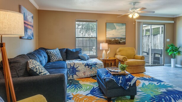 A living room with a sofa, armchair, and ottoman, a large window, and a ceiling fan. - Breezy Fort Walton Townhome ~ 5 Mi to Beach! (Fort Walton Beach)