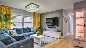 A modern living room with a sectional sofa, a white coffee table, a TV mounted on the wall, and a wooden cabinet with glass doors. - Emerald Coast Vacation Rental: 1 Mi to Beach (Shalimar)