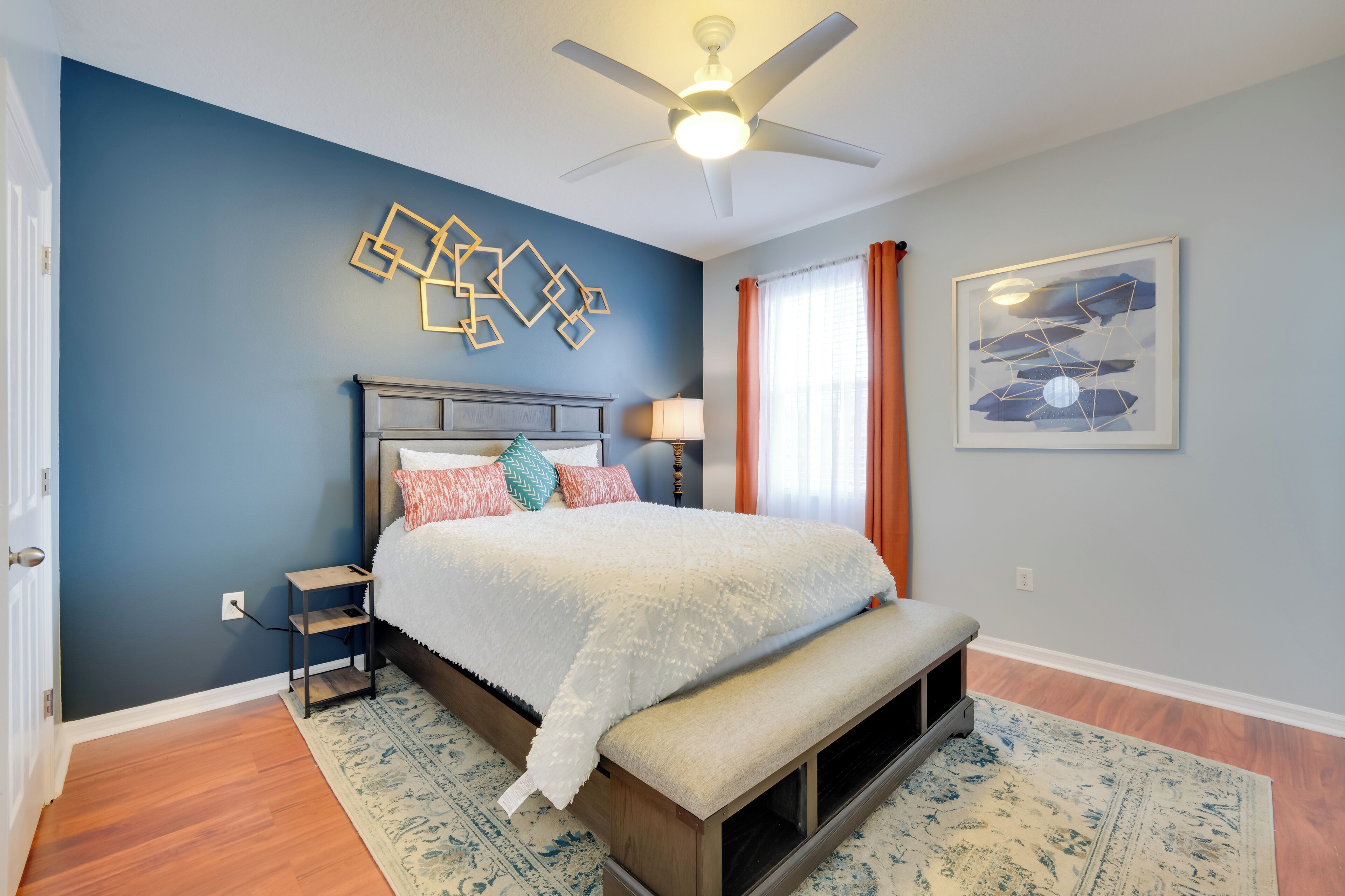 A bedroom with a bed, a ceiling fan, a wall art piece, and a window with curtains.