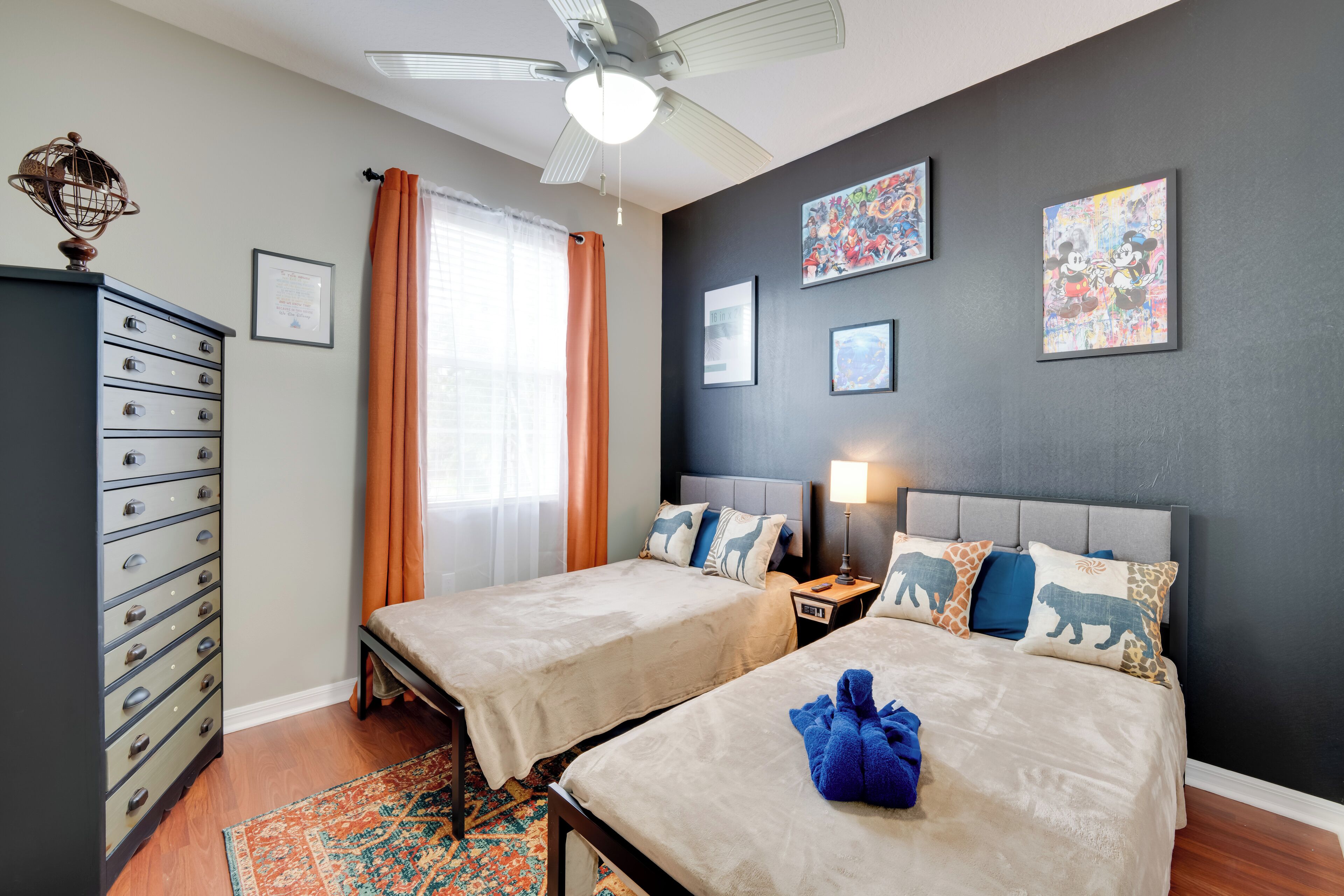 A hotel room with two beds, a dresser, a ceiling fan, and artwork on the walls.